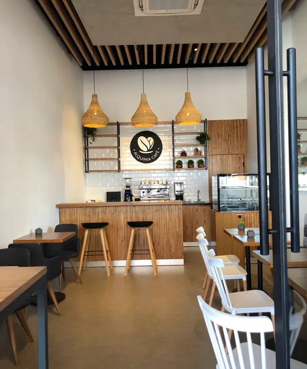 La barra de Alquimia bajo tres lámparas de mimbre, con el logo en la pared