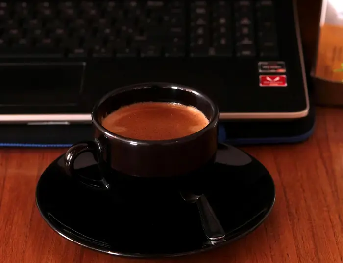 Un café doble en taza negra junto a un teclado