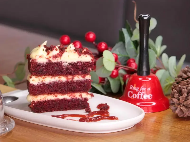 Una porción de Red Velvet de tres capas con crema, en un plato blanco sobre una mesa de madera